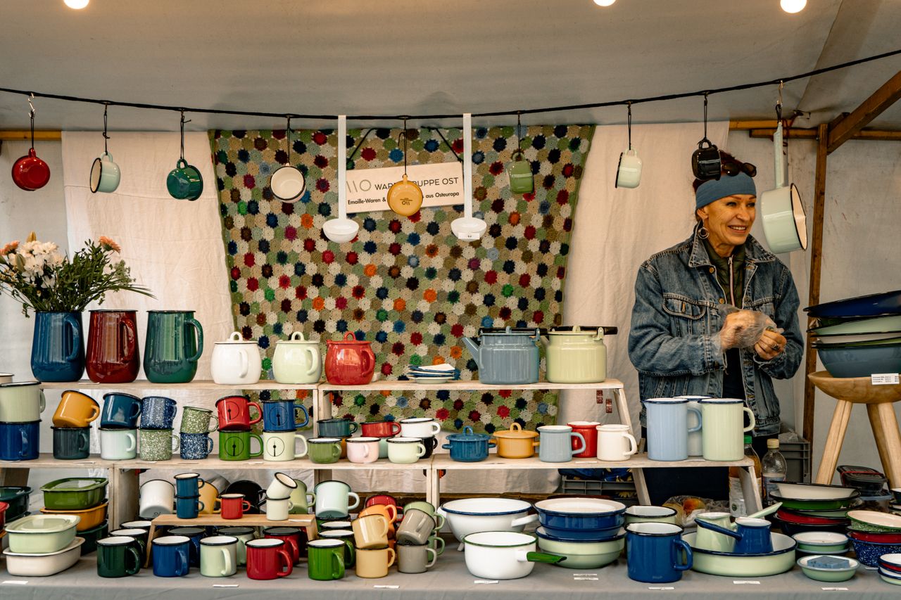 Vibrant display of handmade pottery with a smiling vendor at a market stall.